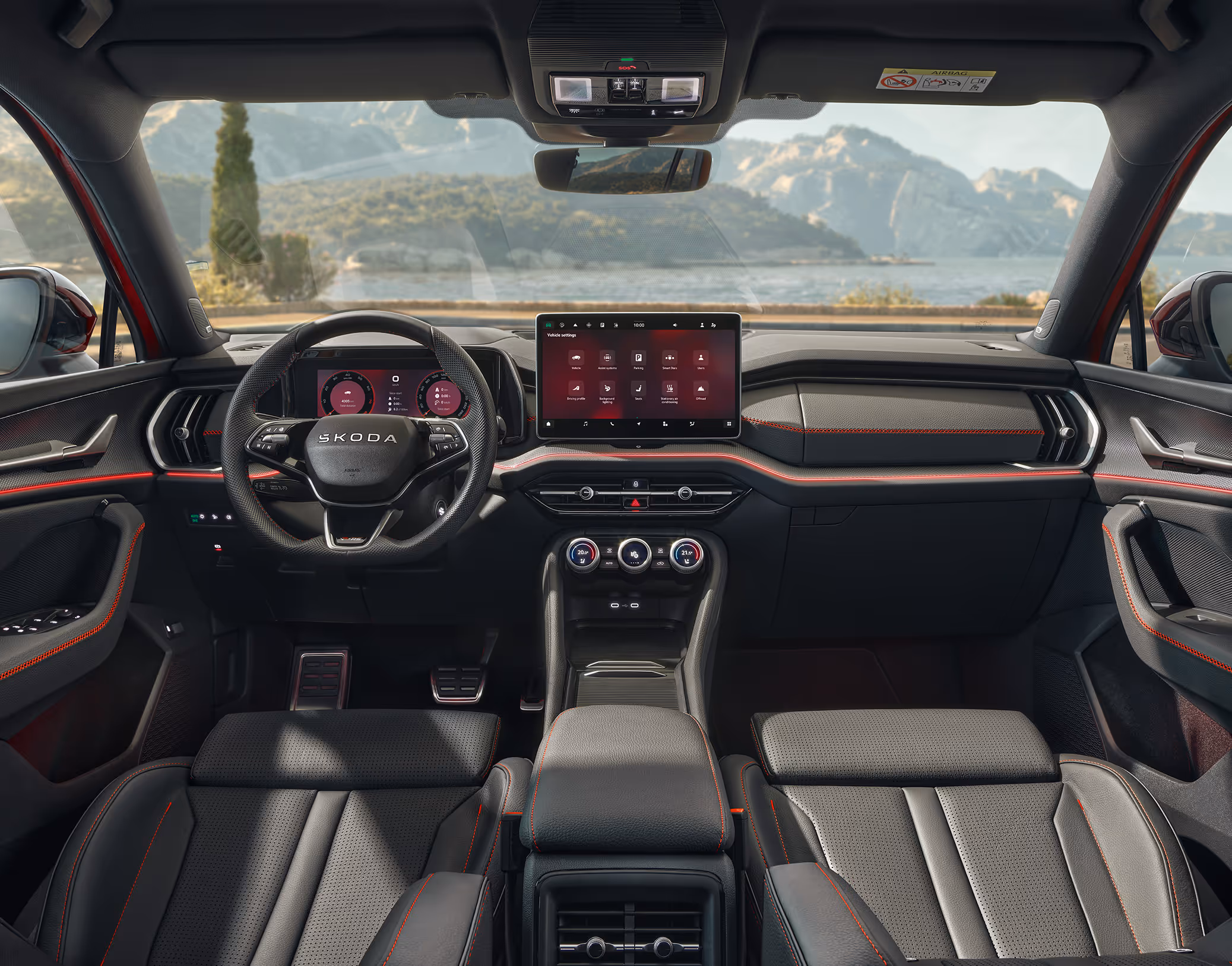 Eine weite Innenansicht aus der Rücksitzperspektive eines Škoda Kodiaq zeigt das gesamte Cockpit mit der Design Selection RS Suite. Das sportliche, dunkle Interieur mit seinen schwarzen Leder-Kunstleder-Sitzbezügen mit roten Kontrastnähten und Dekorleisten in Carbon-Optik steht im Kontrast zur hellen, städtischen Szenerie, die durch die Windschutzscheibe sichtbar ist.