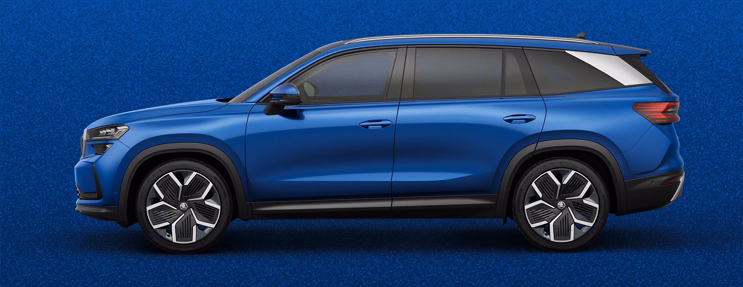 Seitenansicht eines Škoda Kodiaq in der Lackierung Race-Blau Metallic mit 20 Zoll Leichtmetallfelgen “Rila Aero” vor einem einfarbigen Hintergrund in der Farbe der Fahrzeuglackierung.