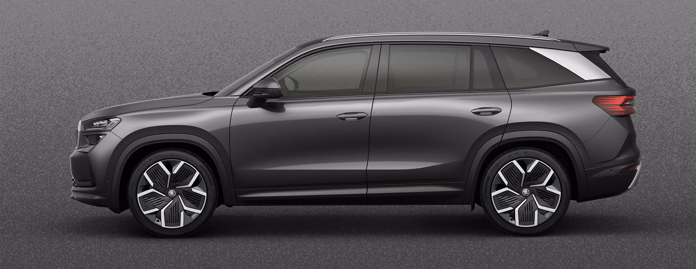 Seitenansicht eines Škoda Kodiaq in der Lackierung Graphite-Grau Metallic mit 20 Zoll Leichtmetallfelgen “Rila Aero” vor einem einfarbigen Hintergrund in der Farbe der Fahrzeuglackierung.