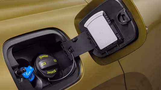 Eine Nahaufnahme zeigt die geöffnete Tankklappe eines Škoda Kodiaq in der Lackierung Gold-Bronze Metallic. Im Inneren sind der schwarze Tankdeckel für den Dieselkraftstoff und der danebenliegende blaue Deckel für den AdBlue-Zusatz zu sehen. An der Innenseite der Klappe ist der integrierte Eiskratzer als praktisches Detail untergebracht.