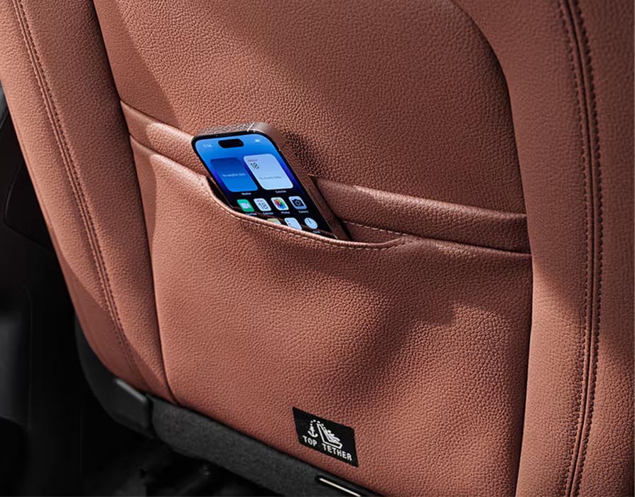 Eine Nahaufnahme zeigt eine der Smartphone-Taschen an der Rückseite eines Vordersitzes im Škoda Kodiaq. Ein Smartphone steckt sicher in der dafür vorgesehenen Tasche, die in den cognac-braunen Lederbezug der Design Selection Lounge integriert ist.
