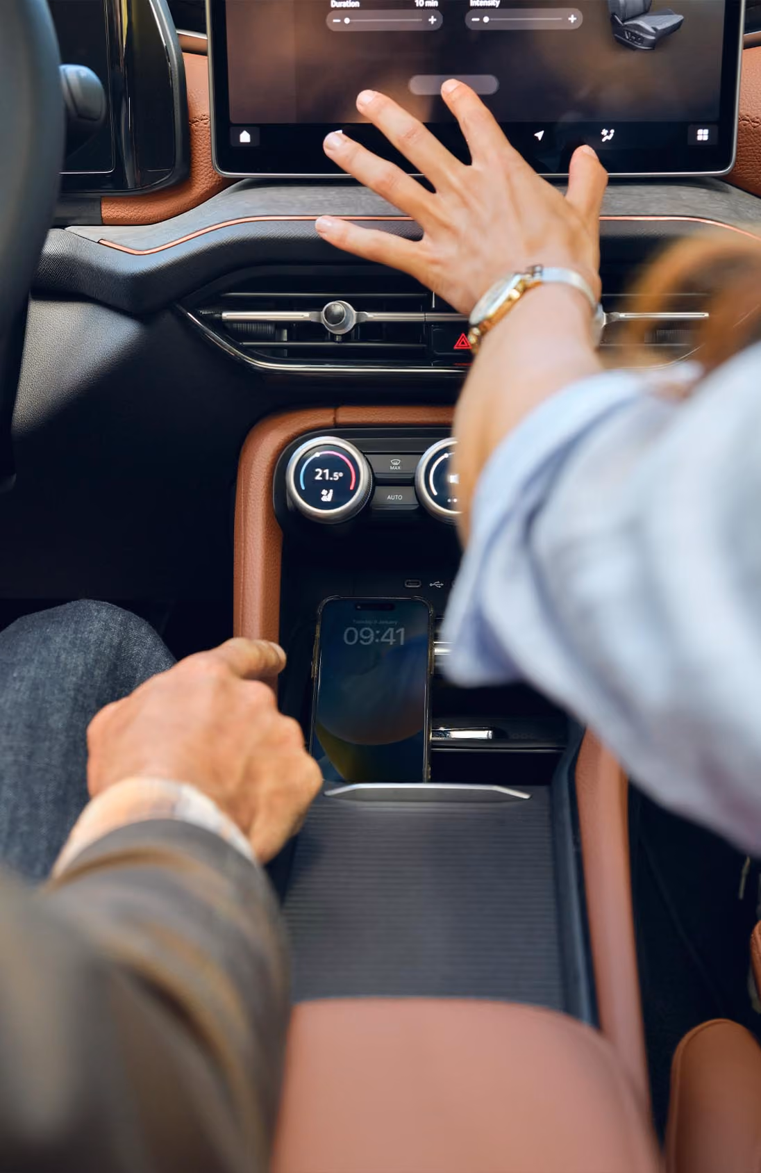Blick von der Rückbank aus auf ein Paar im vorderen Teil eines Škoda Kodiaq. Die Beifahrerin interagiert mit dem großen Infotainmentdisplay und zeigt auf die Navigationskarte, während der Fahrer ebenfalls dorthin schaut. Das Interieur mit den cognac-braunen Ledersitzen der Design Selection Lounge ist stimmungsvoll beleuchtet.  Unten rechts steht auf einer dunkelgrün abgesetzten Fläche geschrieben: "Škoda Connect"