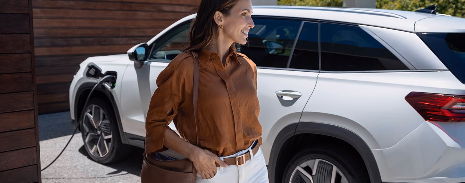 Blick von der Rückbank aus auf ein Paar im vorderen Teil eines Škoda Kodiaq. Der Mann auf dem Fahrersitz hält seiner Partnerin ein Smartphone hin. Die Frau auf dem Beifahrersitz bedient es und die Benutzeroberfläche wird über die kabellose SmartLink-Funktion auf dem großen, zentralen Infotainmentdisplay gespiegelt.