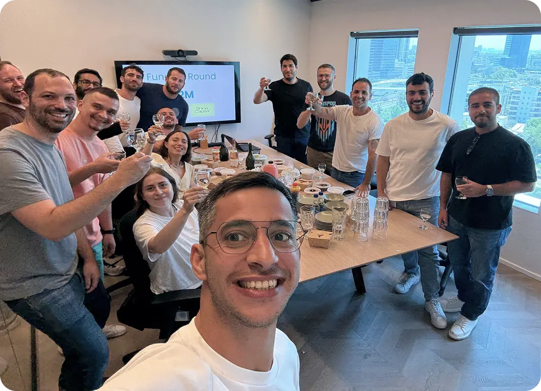 Group of people in an office celebrating and raising glasses around a table with food and drinks.