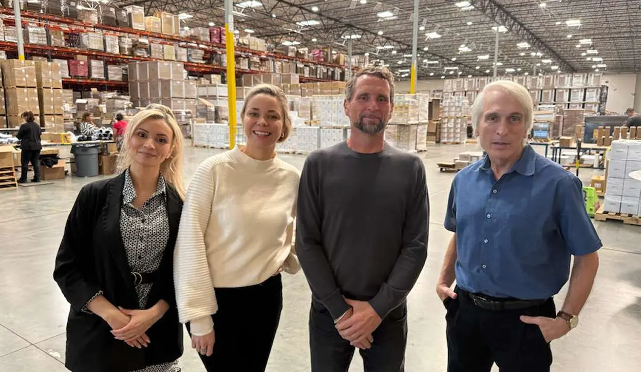Four people standing inside a large warehouse with shelves stacked with boxes behind them.