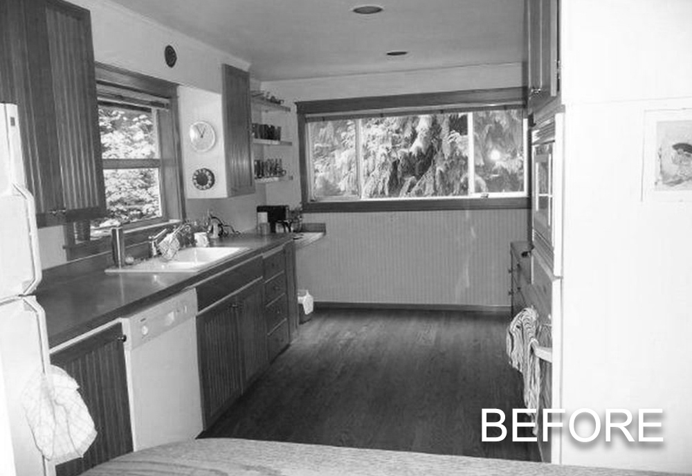 Black and white kitchen interior with wooden cabinets, a sink under a window, and large windows overlooking trees.