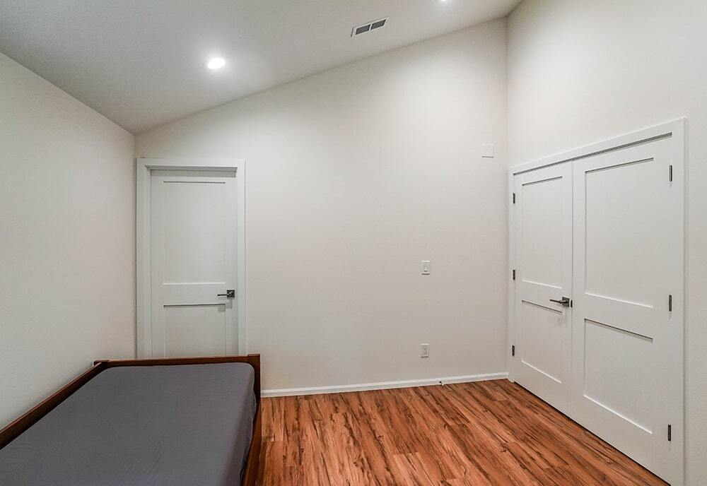 Minimalist room with white vaulted ceiling, wooden floor, a bed with gray bedding, one door, and a double closet door.