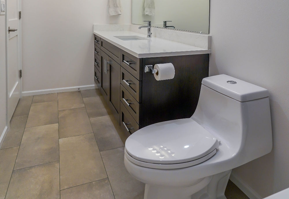 Modern bathroom with white toilet, dark wood vanity with white countertop and chrome faucet, and beige floor tiles.