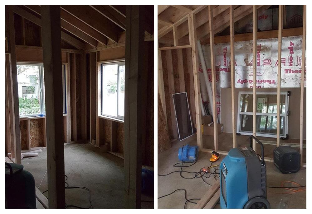 Interior view of a room under construction with exposed wooden framing, windows installed, and construction equipment on the floor.