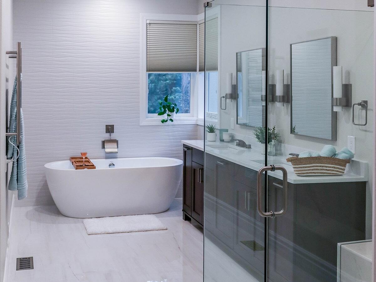 Modern bathroom with a white freestanding bathtub, wooden bath tray, window with blinds, and dark wood vanity with two mirrors and sconces.
