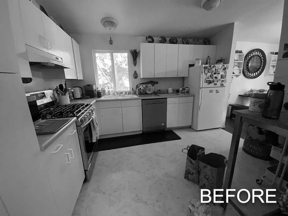 Black and white photo of a cluttered kitchen with white cabinets, a stove, dishwasher, refrigerator, and bags on the floor.