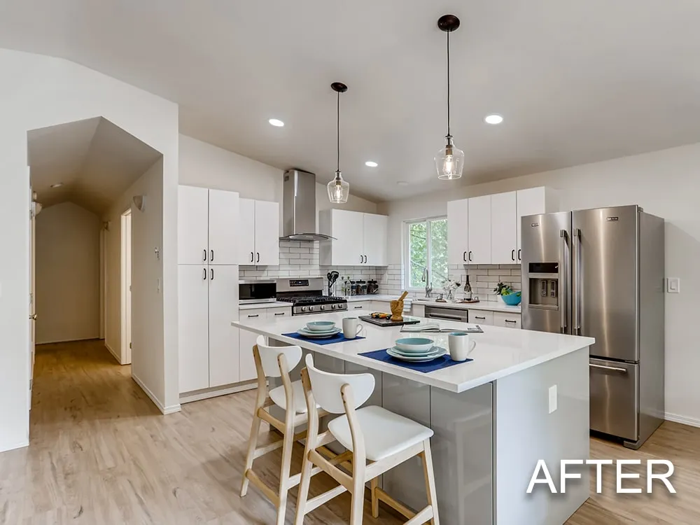 Modern kitchen with white cabinets, stainless steel appliances, a large island with seating for two, and pendant lights.