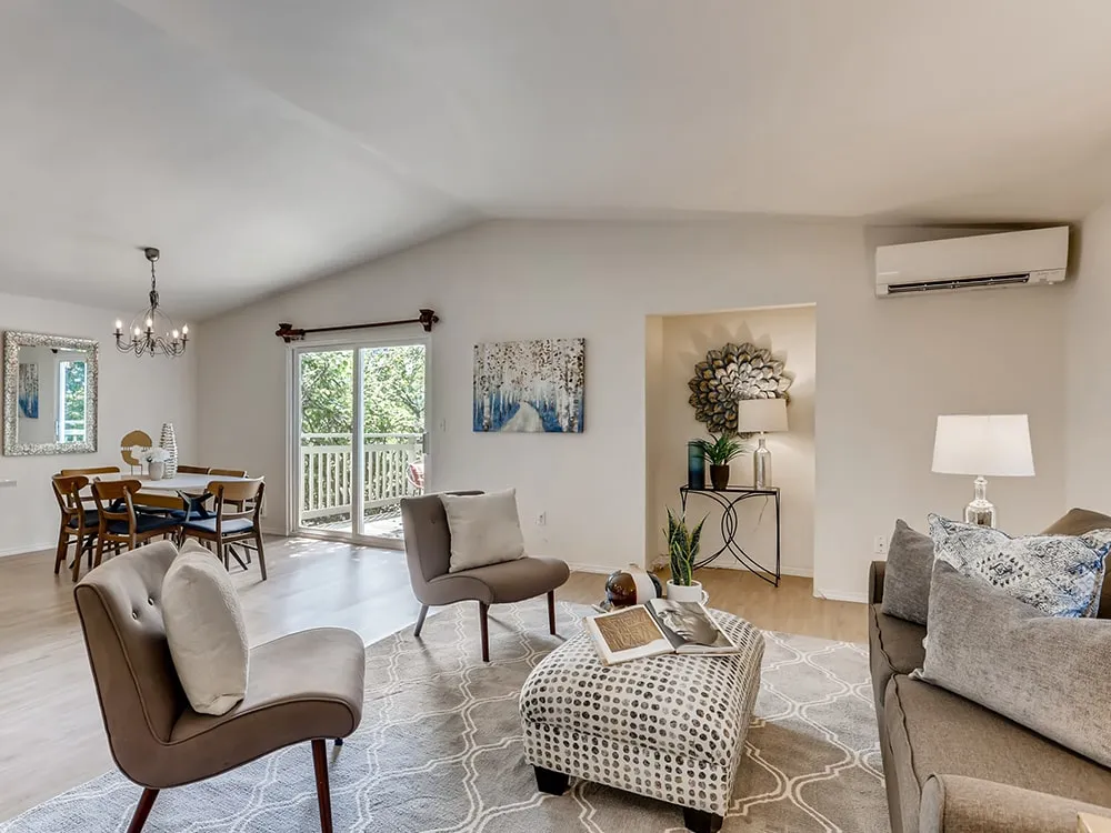 Bright living room and dining area with modern furniture, a large window sliding door, decorative art, and indoor plants.