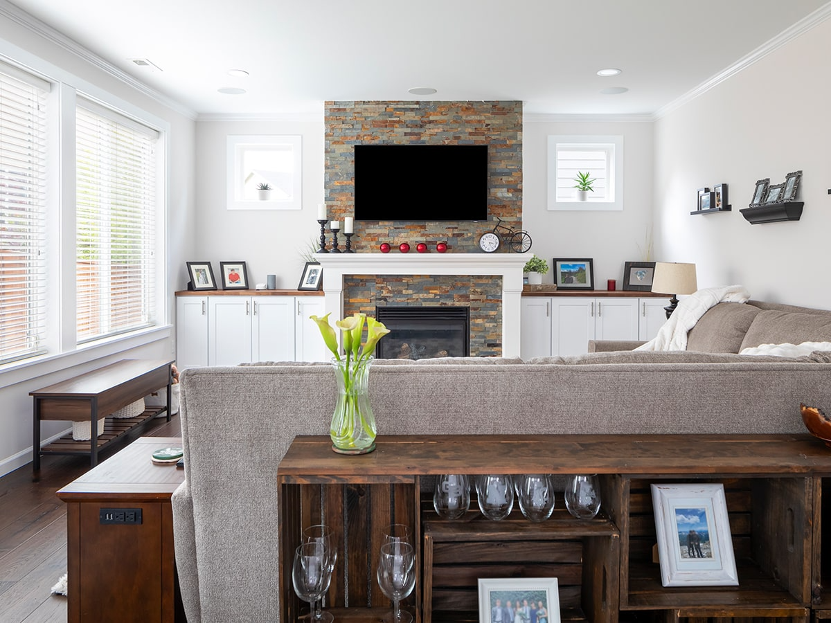 living room design in Everett Washington with white walls, dark wood floor living room renovation, a standard fireplace, a stone fireplace and a wall-mounted tv, a butcher block countertop above the living room storage, white shaker cabinets