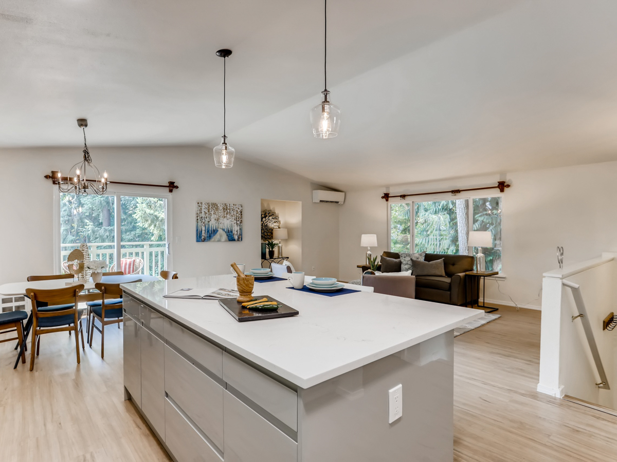 Open-concept modern coastal home remodel with bright kitchen island, pendant lighting, and seamless flow into the living room with large windows and neutral décor.