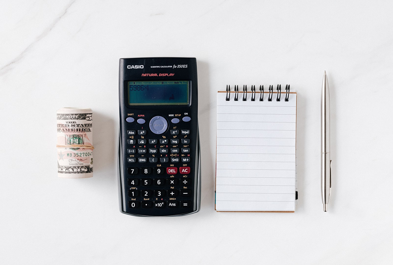 A calculator, pen, bundle of money, and notebook. 
