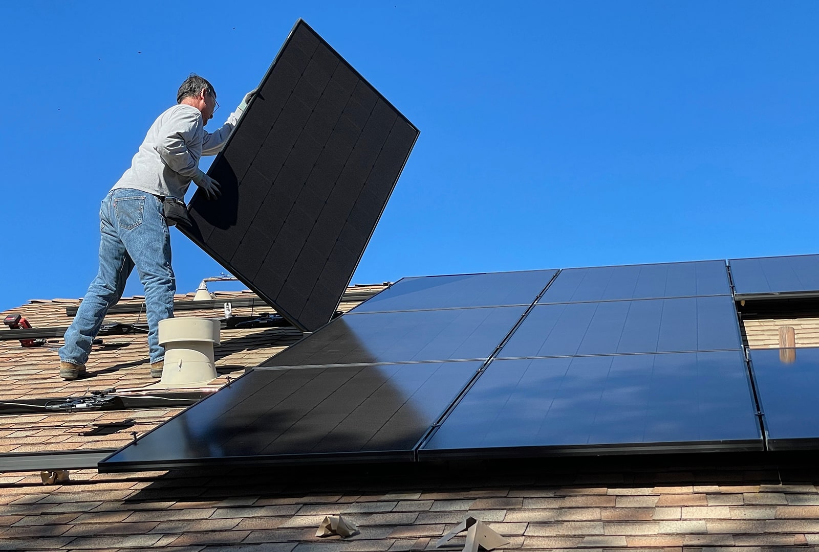 A man installing a big solar panel on the roof.
