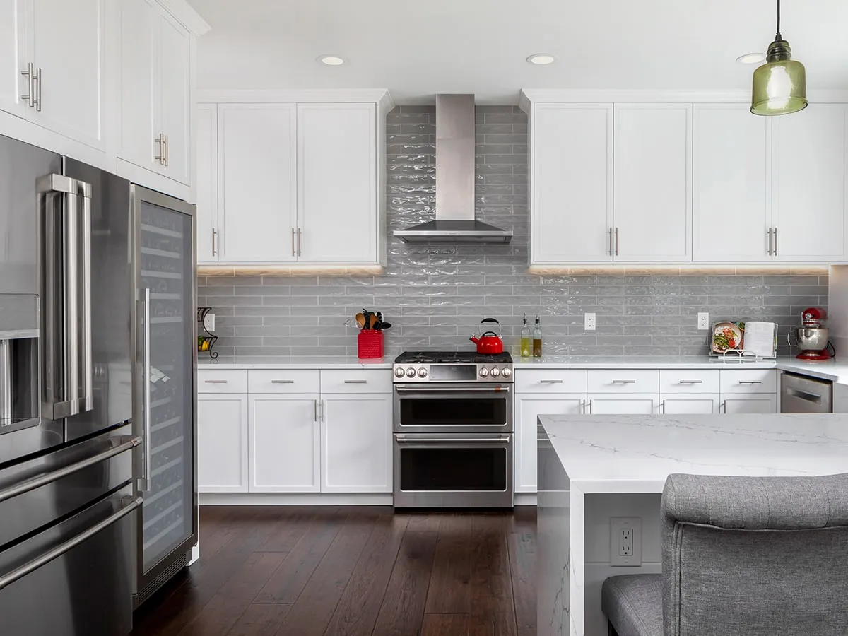 Elegant white kitchen, transitional dark wood floor and brown floor kitchen photo with with apron sink, white cabinets, quartz countertops, waterfall slab on the peninsula, light grey backsplash, subway tile backsplash and stainless steel appliances