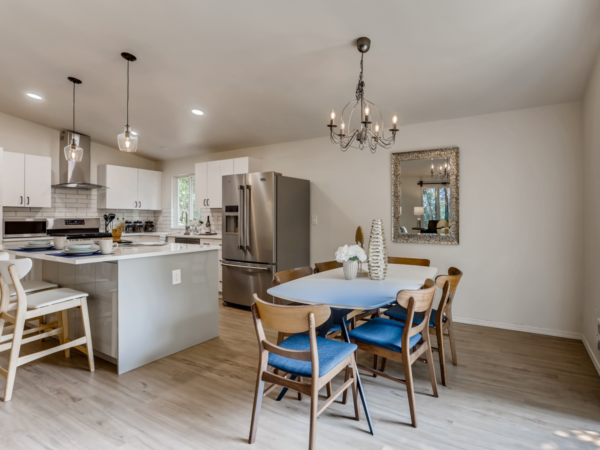 Modern coastal kitchen and dining room remodel featuring white cabinets, quartz countertops, stainless steel appliances, and a rustic chandelier over a wooden dining table.