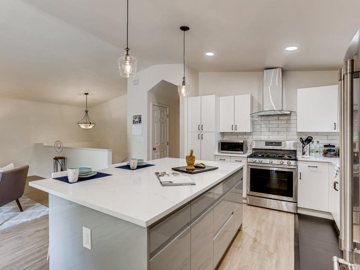 Open-concept modern coastal home remodel with bright kitchen island, pendant lighting, and seamless flow into the living room with large windows and neutral décor.
