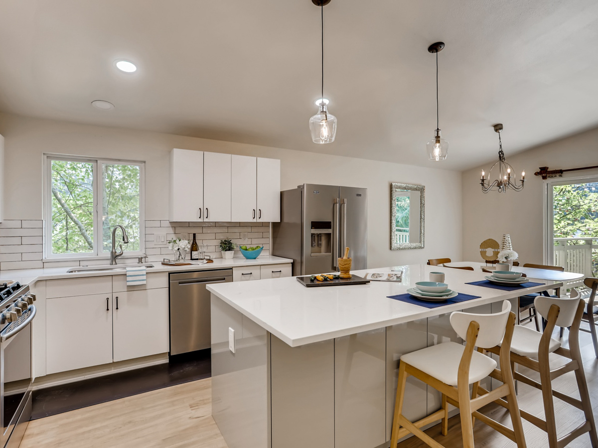 Stylish kitchen renovation with white shaker cabinets, stainless steel fridge, and breakfast bar seating on a sleek white quartz