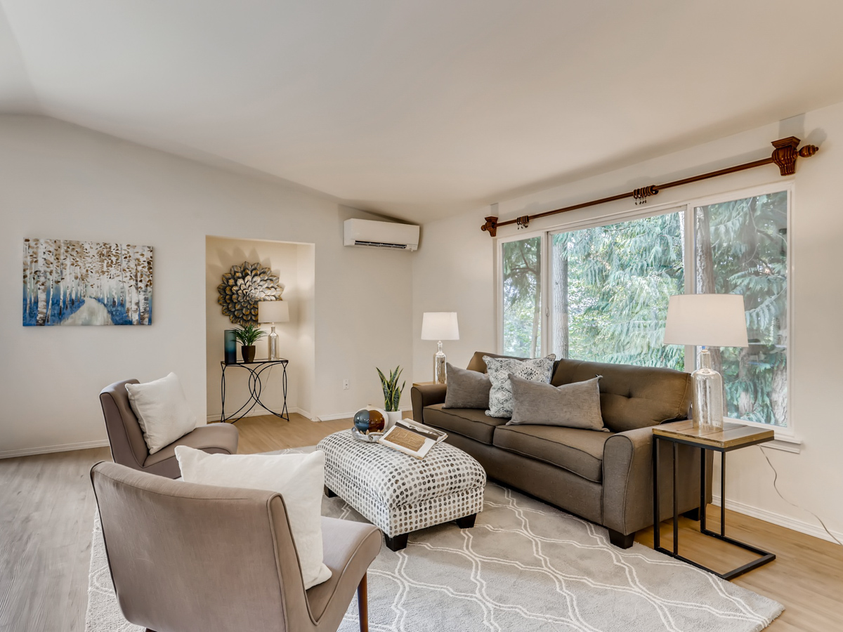 Cozy modern coastal living room featuring large picture windows, beige sofa, accent chairs, and contemporary décor for a light and airy atmosphere.