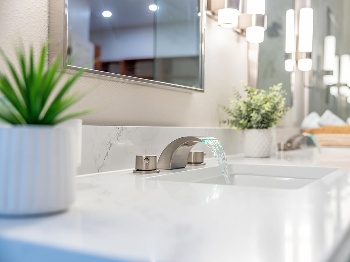 Elegant bathroom vanity with waterfall faucet, quartz countertop, and modern chrome fixtures in a classic-contemporary bathroom remodel.