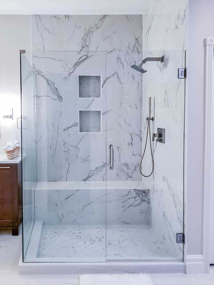 Luxury walk-in shower with glass enclosure and marble tile walls featuring built-in niches and brushed nickel fixtures in a contemporary bathroom design.