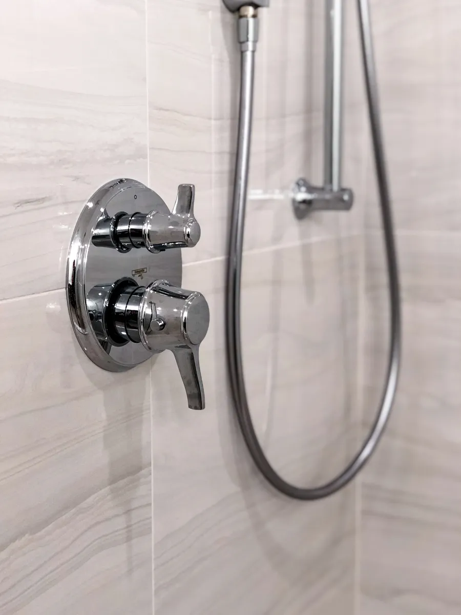 Close-up of modern chrome shower controls and handheld shower hose mounted on gray tile wall.
