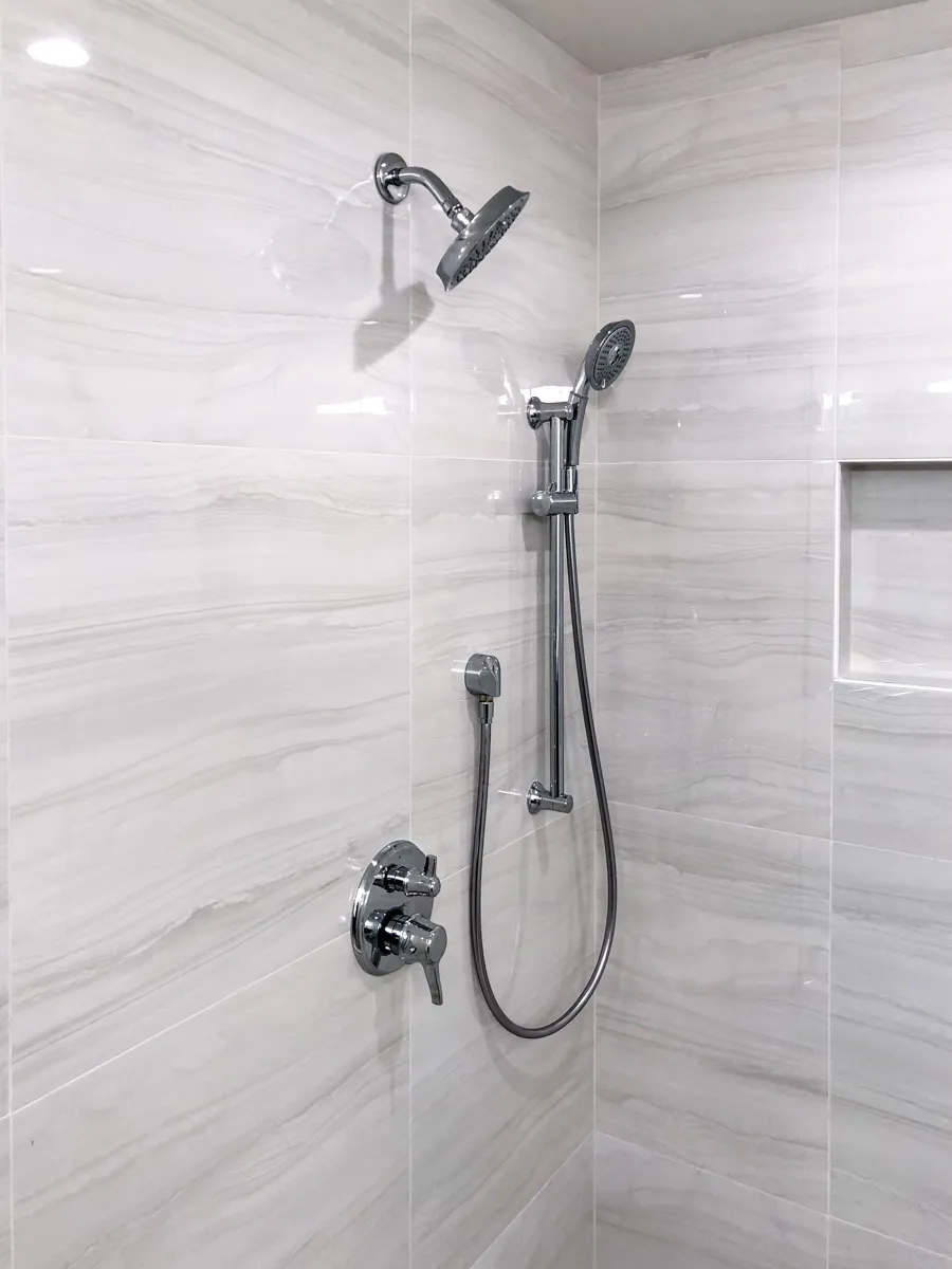 Walk-in shower featuring chrome rainfall showerhead, handheld sprayer, and large gray porcelain wall tiles.