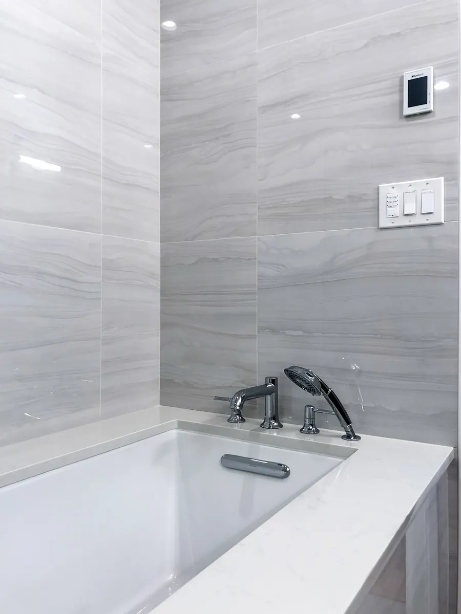 Luxury bathroom with deep soaking tub, chrome fixtures, and large gray marble-look wall tiles