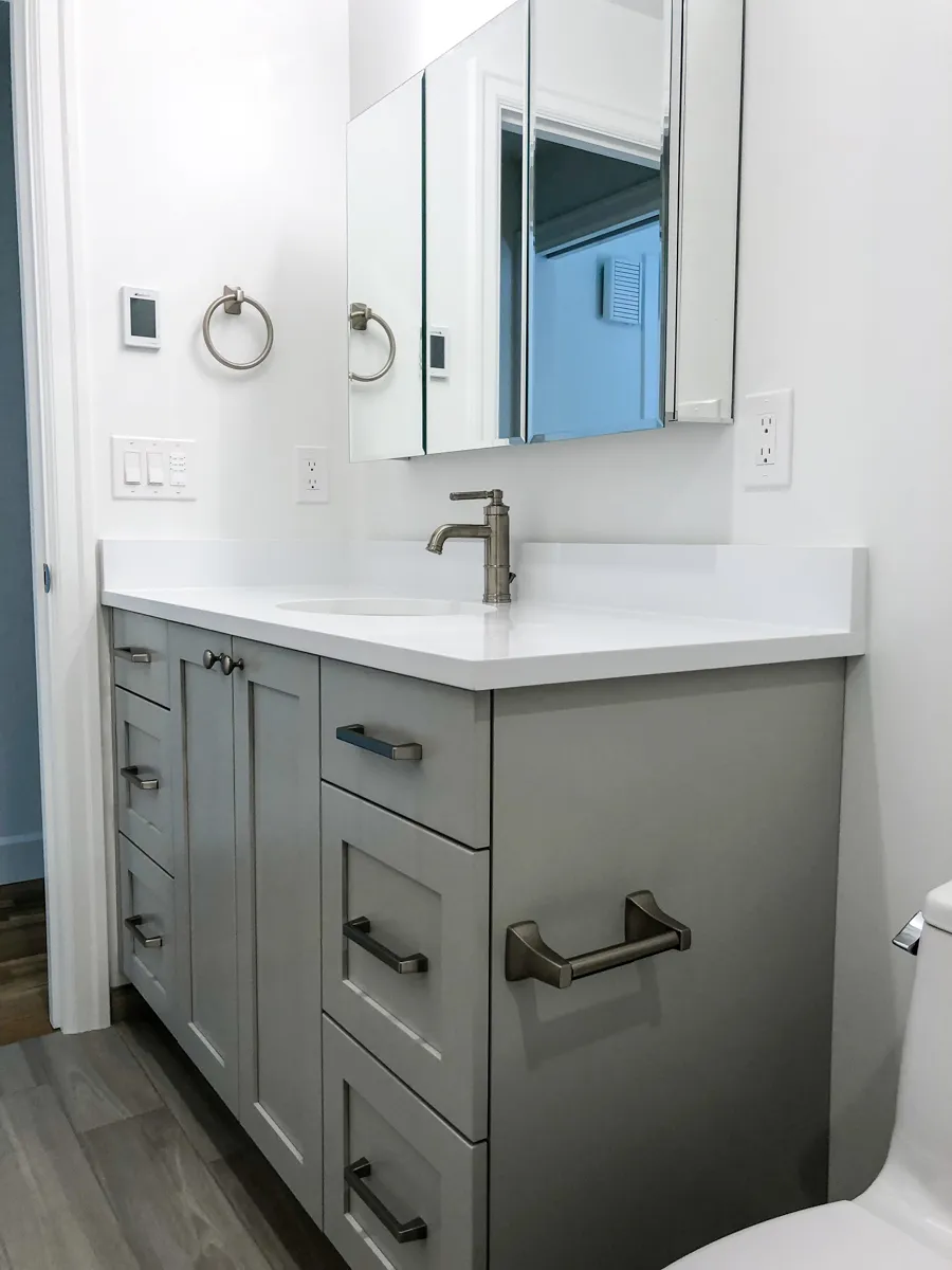 Bathroom with gray shaker vanity cabinets, wood-look tile flooring, and white textured bathtub surround