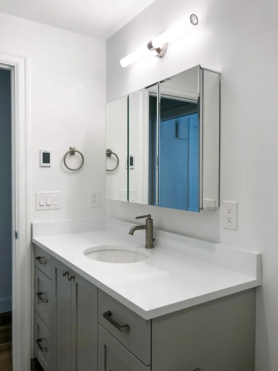Bathroom with gray shaker vanity cabinets, wood-look tile flooring, and white textured bathtub surround