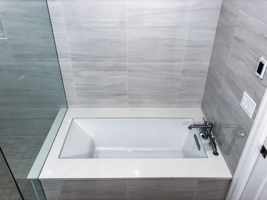 Overhead view of a rectangular soaking tub with chrome fixtures surrounded by gray marble-look tile