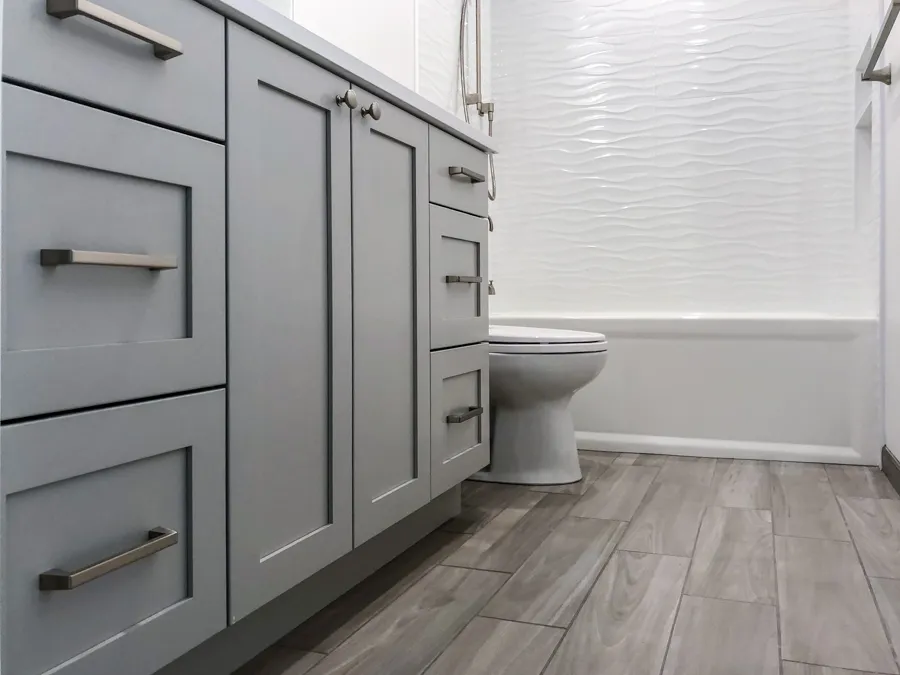Bathroom with gray shaker vanity cabinets, wood-look tile flooring, and white textured bathtub surround