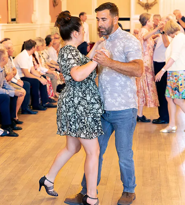 A couple dancing closely in a room with seated and standing people in the background.