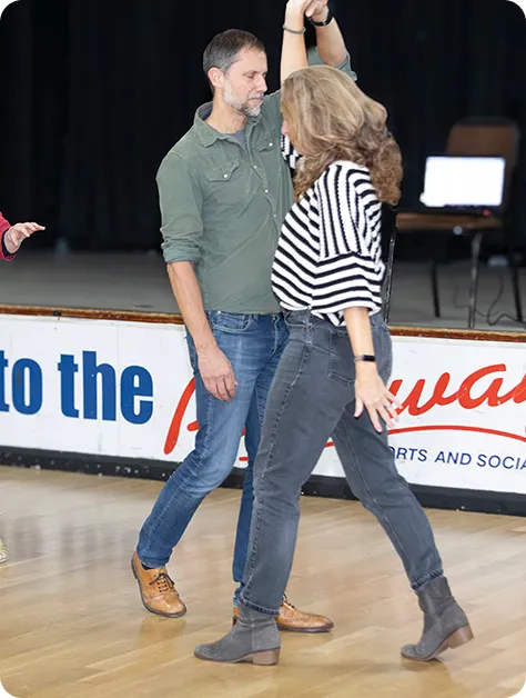 A man and woman dancing together on a wooden floor with a black curtain background.