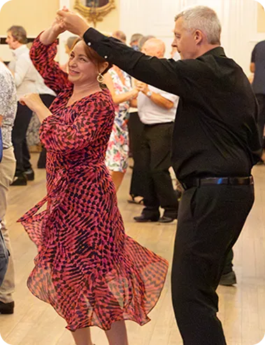 A man and woman smiling and dancing together in a room with other dancing couples.