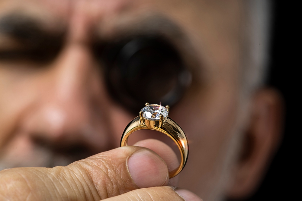 Jewelry appraiser examines a gold ring evaluating large diamond looking through magnifying glass monocular.