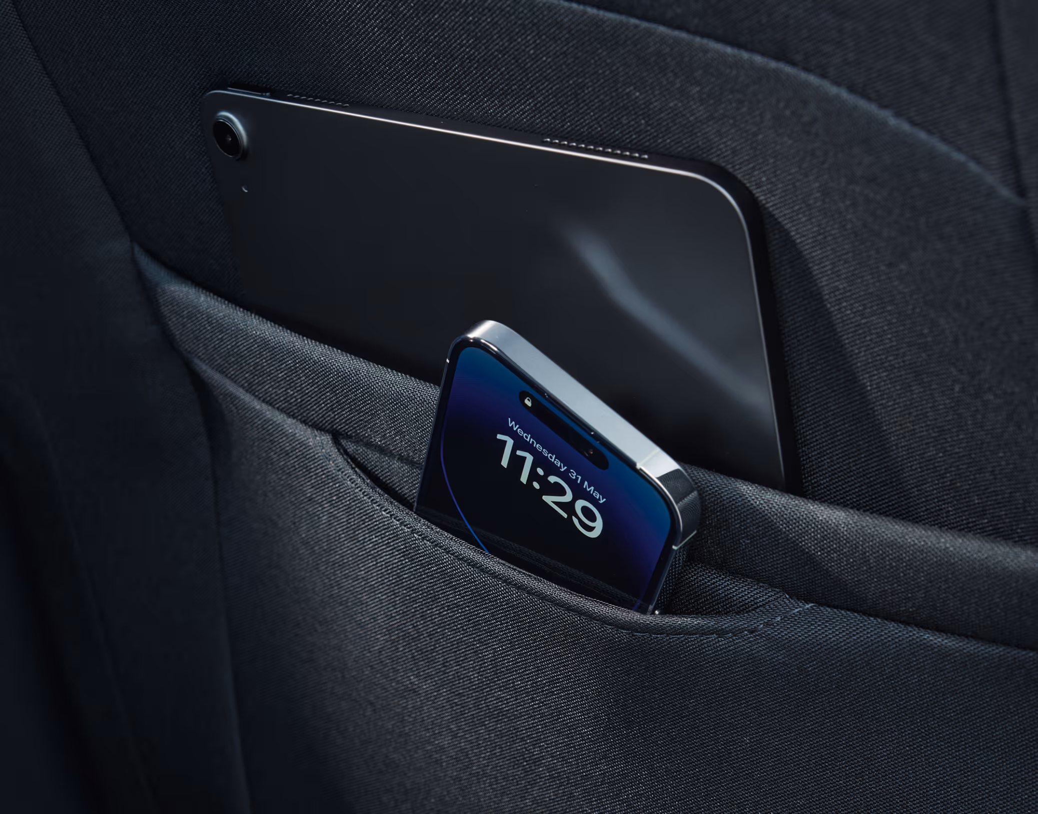 Eine Nahaufnahme zeigt die Ablagetaschen an der Rückseite eines Vordersitzes im Škoda Scala. Ein Smartphone mit eingeschaltetem Display steckt in der vorderen, kleineren Tasche, während ein größeres Gerät, wie ein Tablet, in der Tasche dahinter platziert ist.