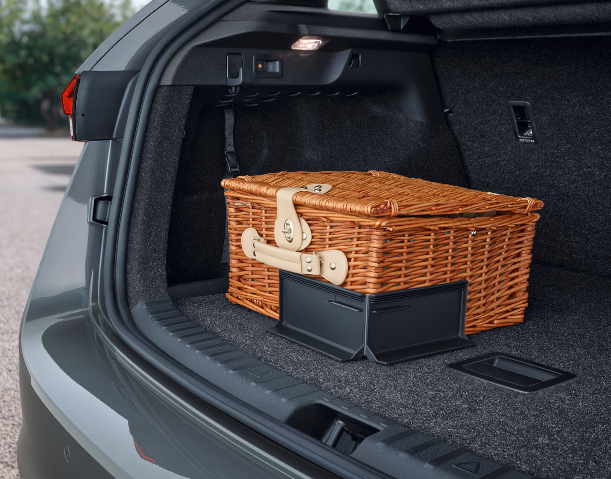 Eine Nahaufnahme des geöffneten Kofferraums eines Škoda Scala zeigt einen Weiden-Picknickkorb, der durch ein aufgestelltes Cargo-Element aus Kunststoff auf dem Kofferraumteppich gesichert wird. Die seitliche Kofferraumbeleuchtung ist eingeschaltet und erhellt den Laderaum.