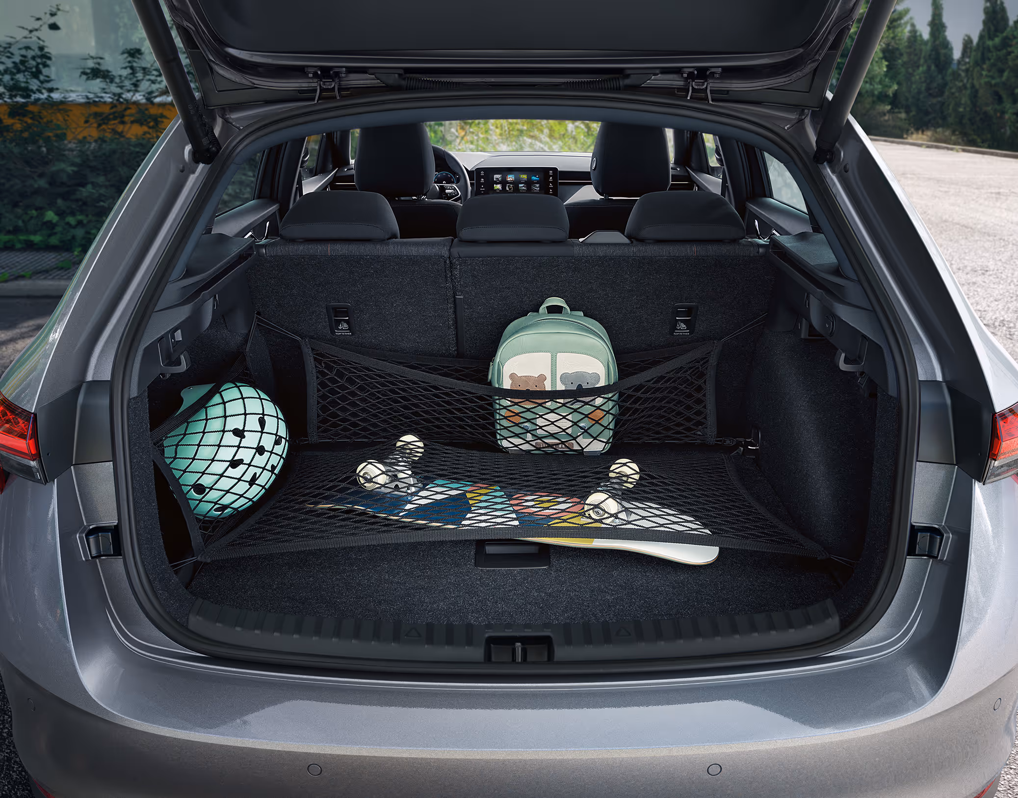 Eine Ansicht des geöffneten Kofferraums eines Škoda Scala zeigt die Anwendung des Netzprogramms. Ein Skateboard wird von einem Bodennetz gesichert, während ein Kinderrucksack in einem Netz an der Rücksitzlehne und ein Helm in einem Seitennetz verstaut sind.