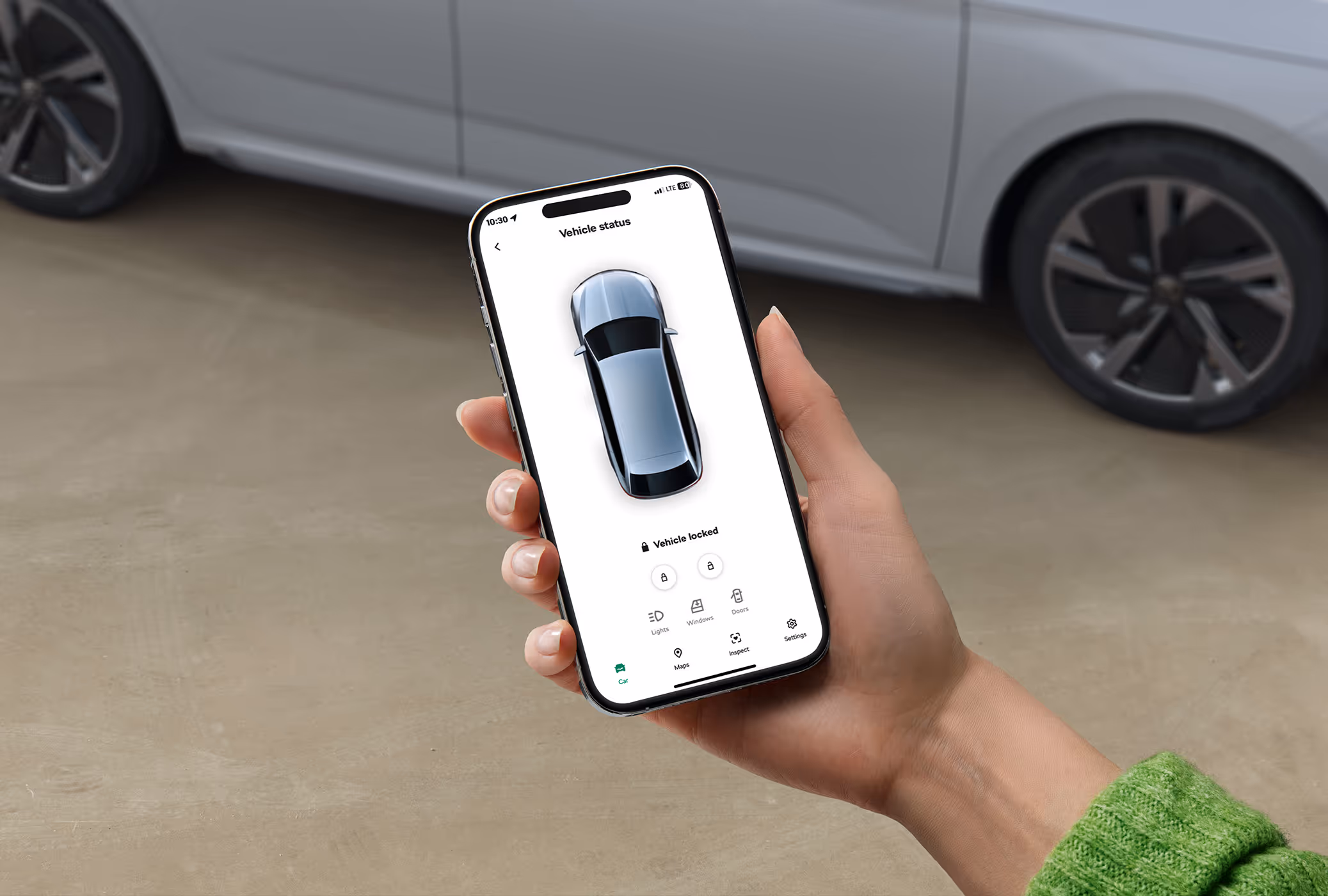 Eine Nahaufnahme zeigt eine Hand, die ein Smartphone mit der geöffneten MyŠKODA App hält. Auf dem Bildschirm wird der Fahrzeugstatus angezeigt, der mit einer Draufsicht des Autos und dem Text „Vehicle locked“ bestätigt, dass das Fahrzeug verriegelt ist. Im unscharfen Hintergrund ist ein Teil des geparkten Škoda Scala zu erkennen.