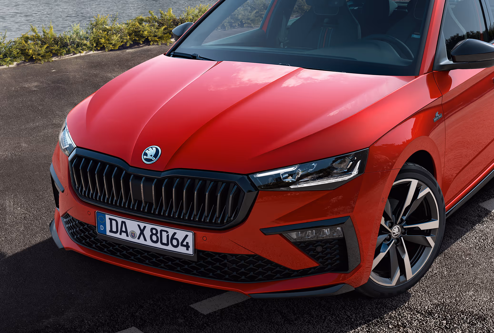Eine Nahaufnahme zeigt die Frontpartie eines Škoda Scala Monte Carlo in der Lackierung Velvet-Rot Metallic. Die Aufnahme hebt die sportlichen Details wie den glänzend schwarzen Kühlergrill, die TOP LED-Matrix-Scheinwerfer und die Monte-Carlo-Plakette am Kotflügel hervor.