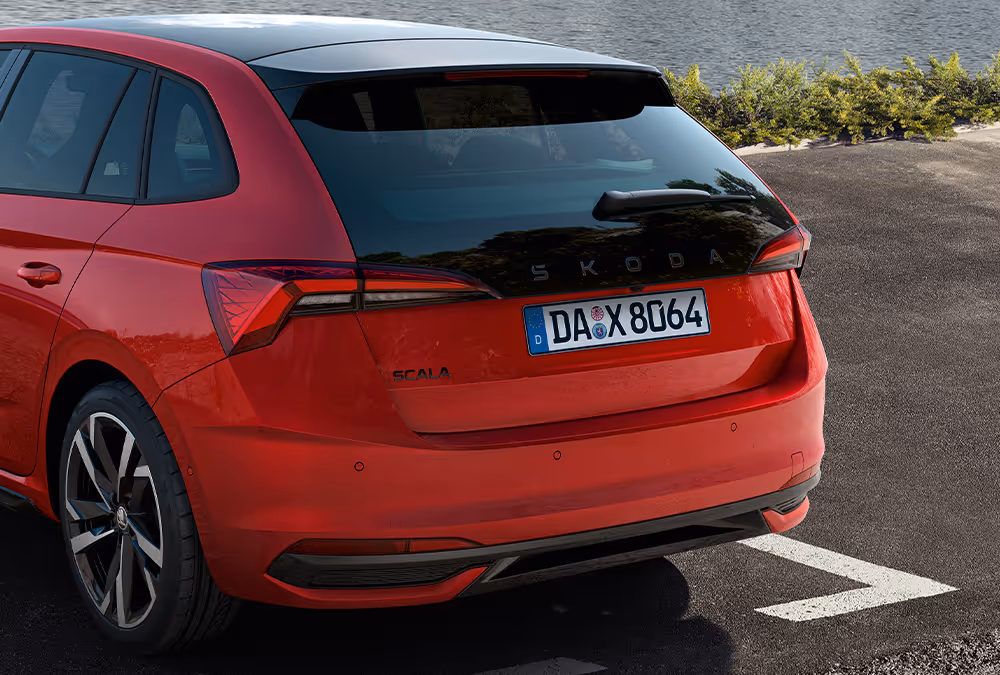 Eine Nahaufnahme zeigt die Heckpartie eines Škoda Scala Monte Carlo in der Lackierung Velvet-Rot Metallic. Die Aufnahme hebt das sportliche Heckdesign mit der verlängerten, schwarzen Heckscheibe, dem schwarzen Škoda Schriftzug und den TOP LED-Heckleuchten hervor.