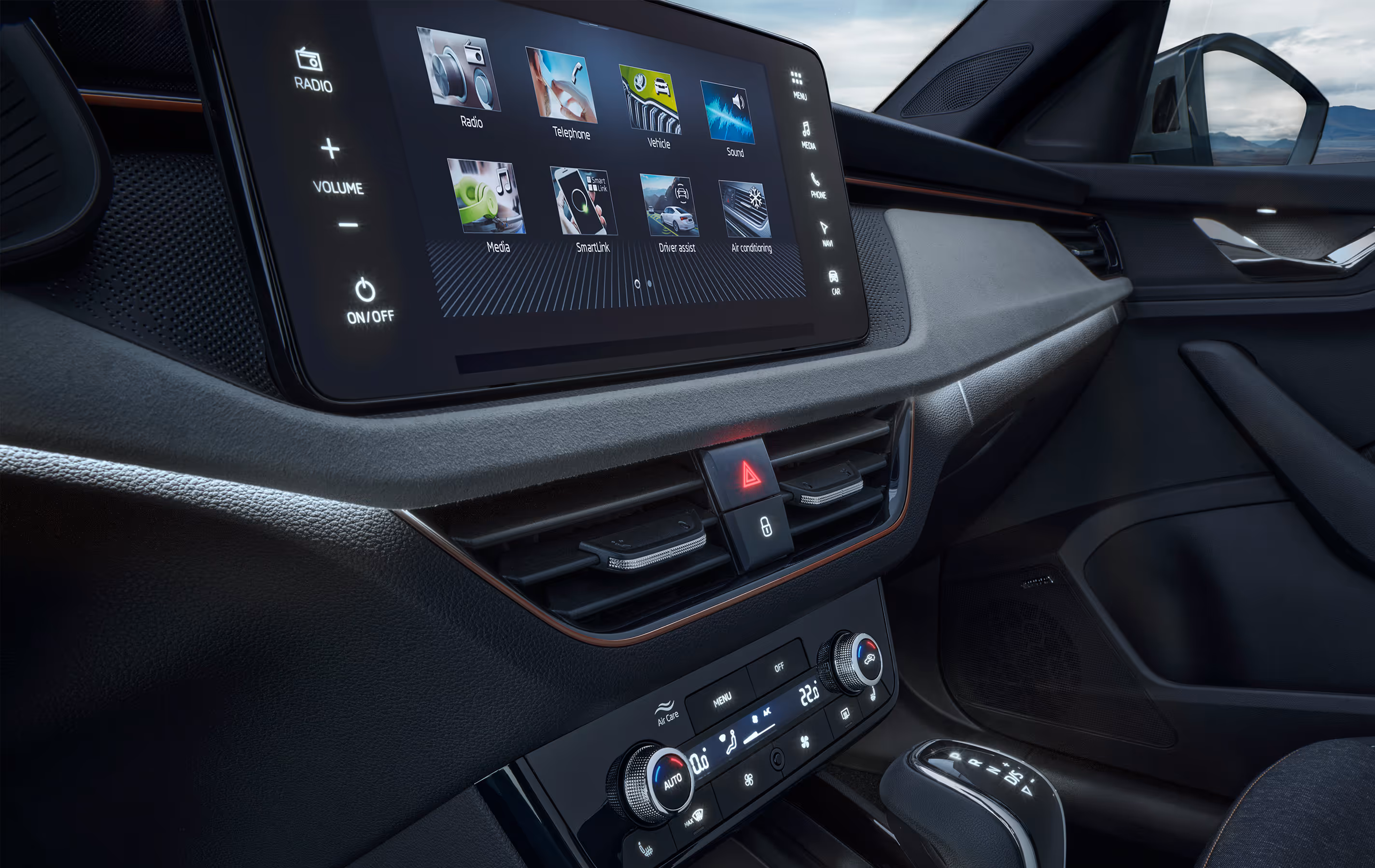 Eine seitliche Innenansicht des Cockpits eines Škoda Scala zeigt das Armaturenbrett mit der Design Selection Lodge. Die Aufnahme hebt die hellgraue, strukturierte Dekorleiste mit dem kupferfarbenen Akzent und das freistehende Infotainment-Display hervor, auf dem das Hauptmenü zu sehen ist.