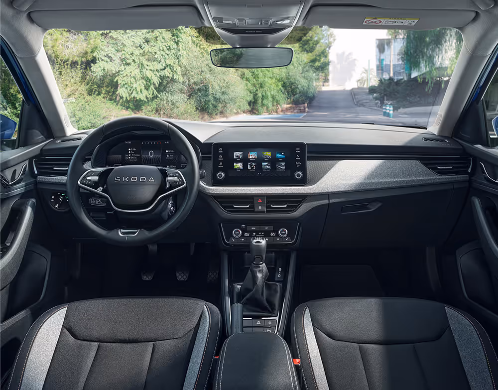 Eine weite Innenansicht zeigt das gesamte Cockpit eines Škoda Scala mit der Design Selection Loft. Das Interieur ist mit Stoffsitzen mit grauen Akzenten und einer hellgrauen, strukturierten Dekorleiste am Armaturenbrett ausgestattet.