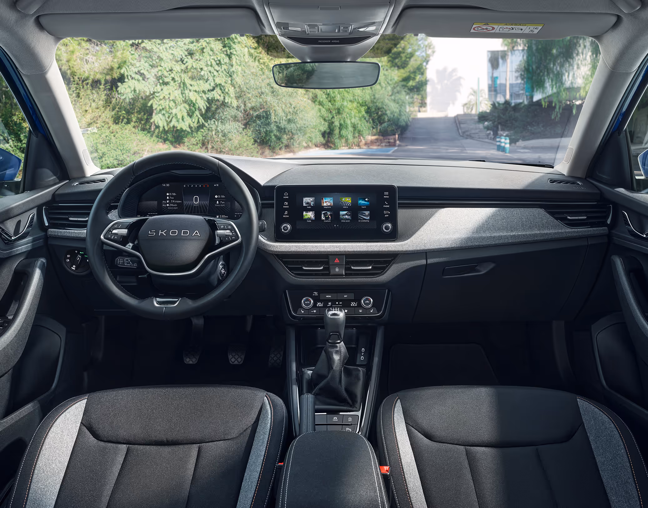 Eine weite Innenansicht zeigt das gesamte Cockpit eines Škoda Scala mit der Design Selection Loft. Das Interieur ist mit Stoffsitzen mit grauen Akzenten und einer hellgrauen, strukturierten Dekorleiste am Armaturenbrett ausgestattet.