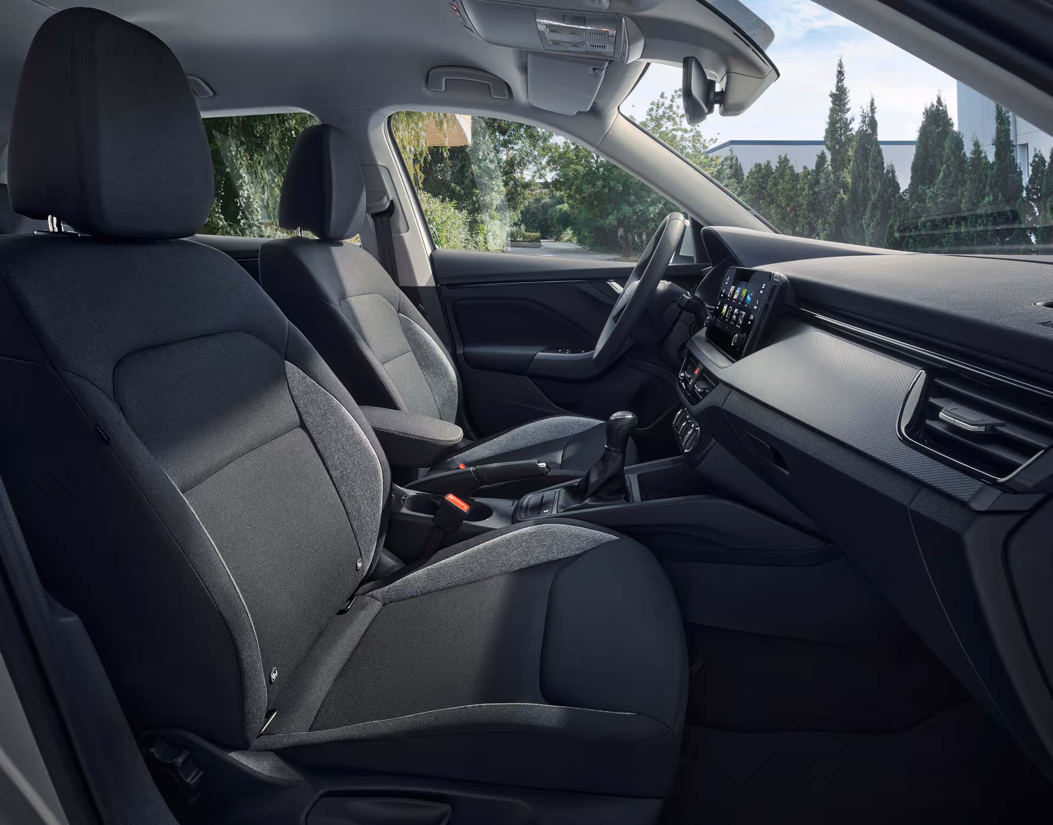 Eine seitliche Innenansicht des Škoda Scala zeigt die Vordersitze und das Cockpit mit der Design Selection Studio. Die Sitzbezüge kombinieren schwarzen Stoff mit grauen Stoffeinsätzen an den Seitenwangen und werden durch helle Kontrastnähte akzentuiert.