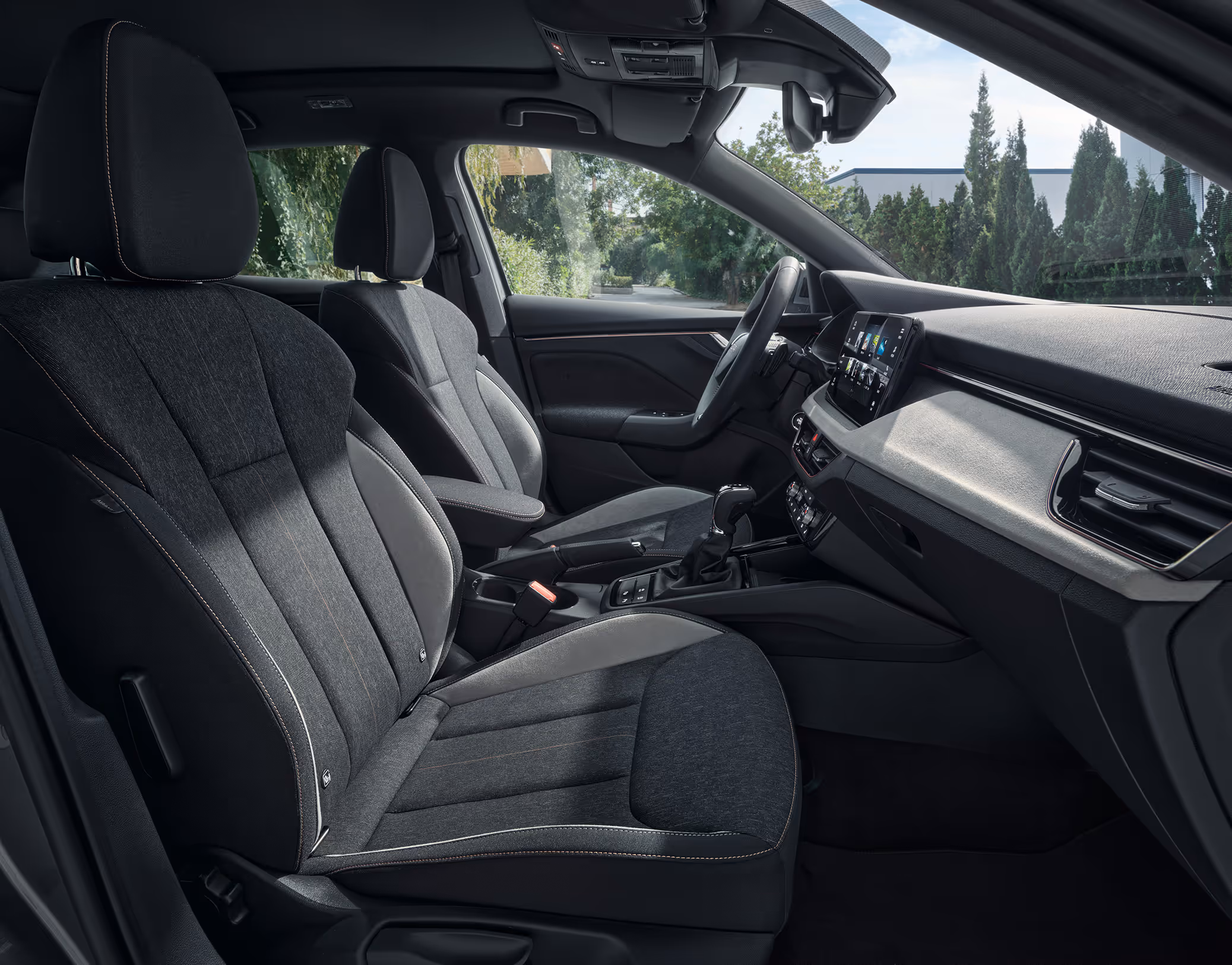 Eine seitliche Innenansicht des Škoda Scala zeigt die Vordersitze und das Cockpit mit der Design Selection Lodge. Die Sitzbezüge kombinieren schwarzen Stoff mit grauem Microfaser-Stoff (Suedia) an den Seitenwangen und werden durch kupferfarbene Kontrastnähte akzentuiert.